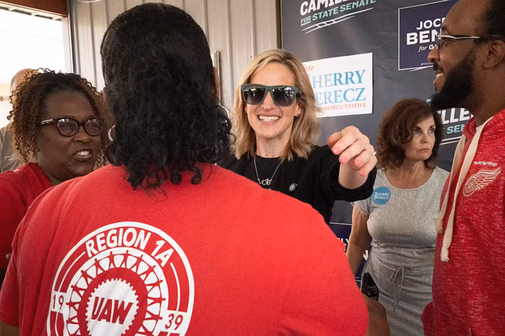 A woman wearing sunglasses smiles at a woman wearing a red t-shirt.